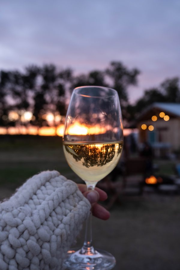 A glass of wine held up in front of the sun setting.