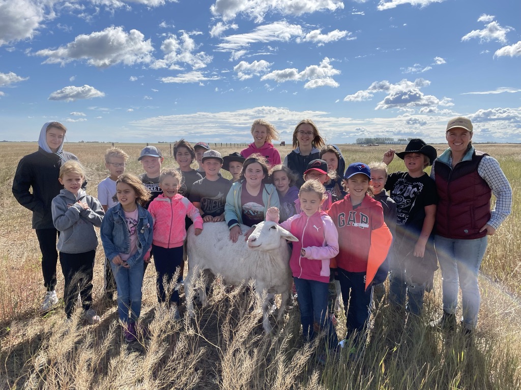 A group shot of kids in a field with a sheep in front.